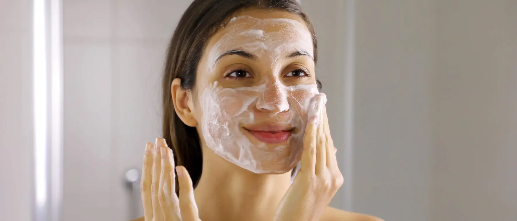 Woman applying foamy facial cleanser in bathroom